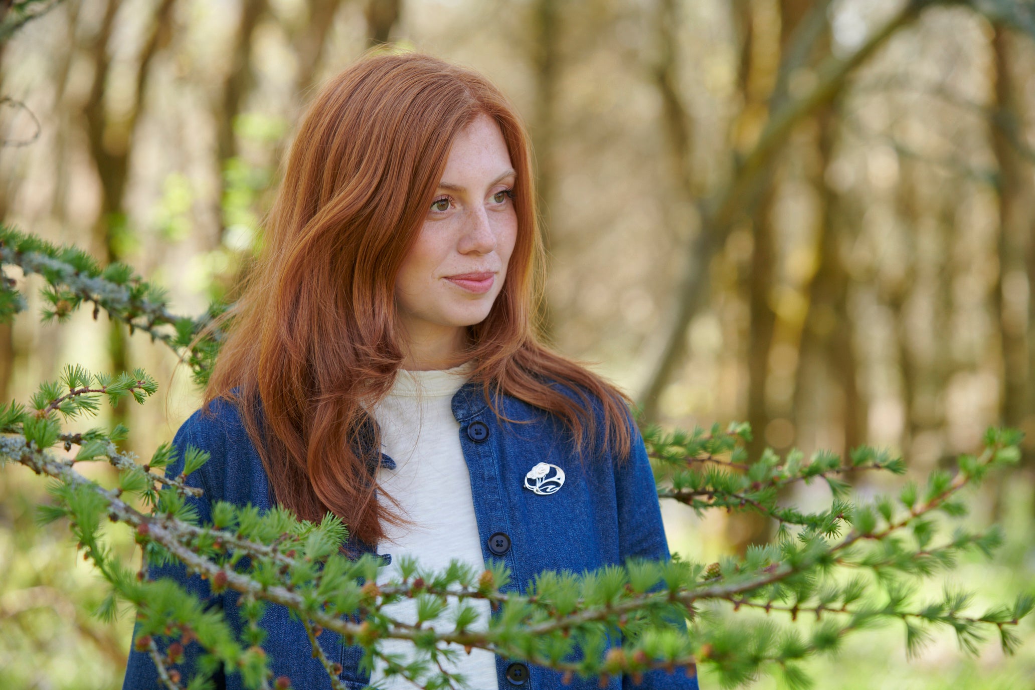 Woman in blue jacket standing behind branch wearing Happy Valley brooch