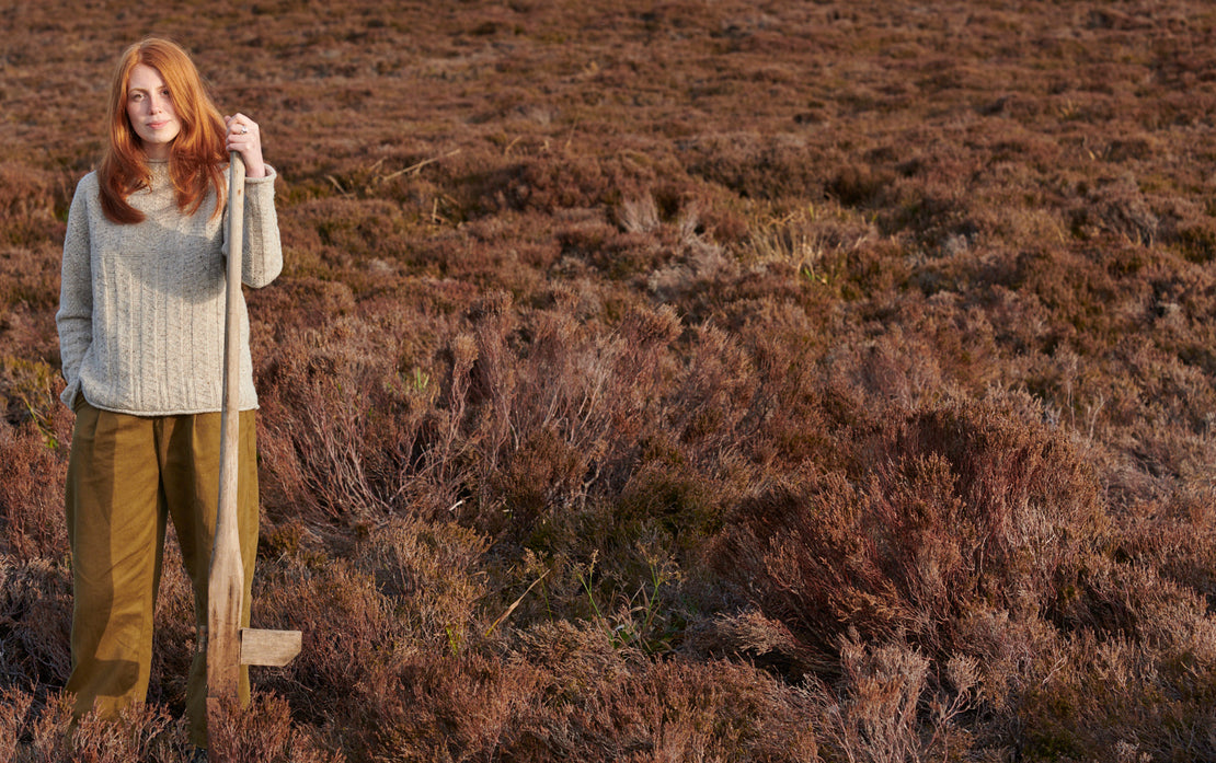 Woman standing in heather holding a peat cutter