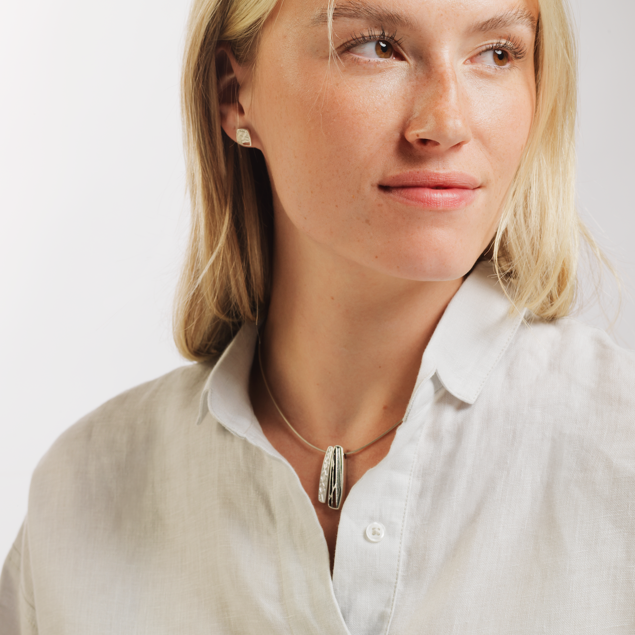 Woman in white shirt wearing ness of brodgar necklace and stud earring