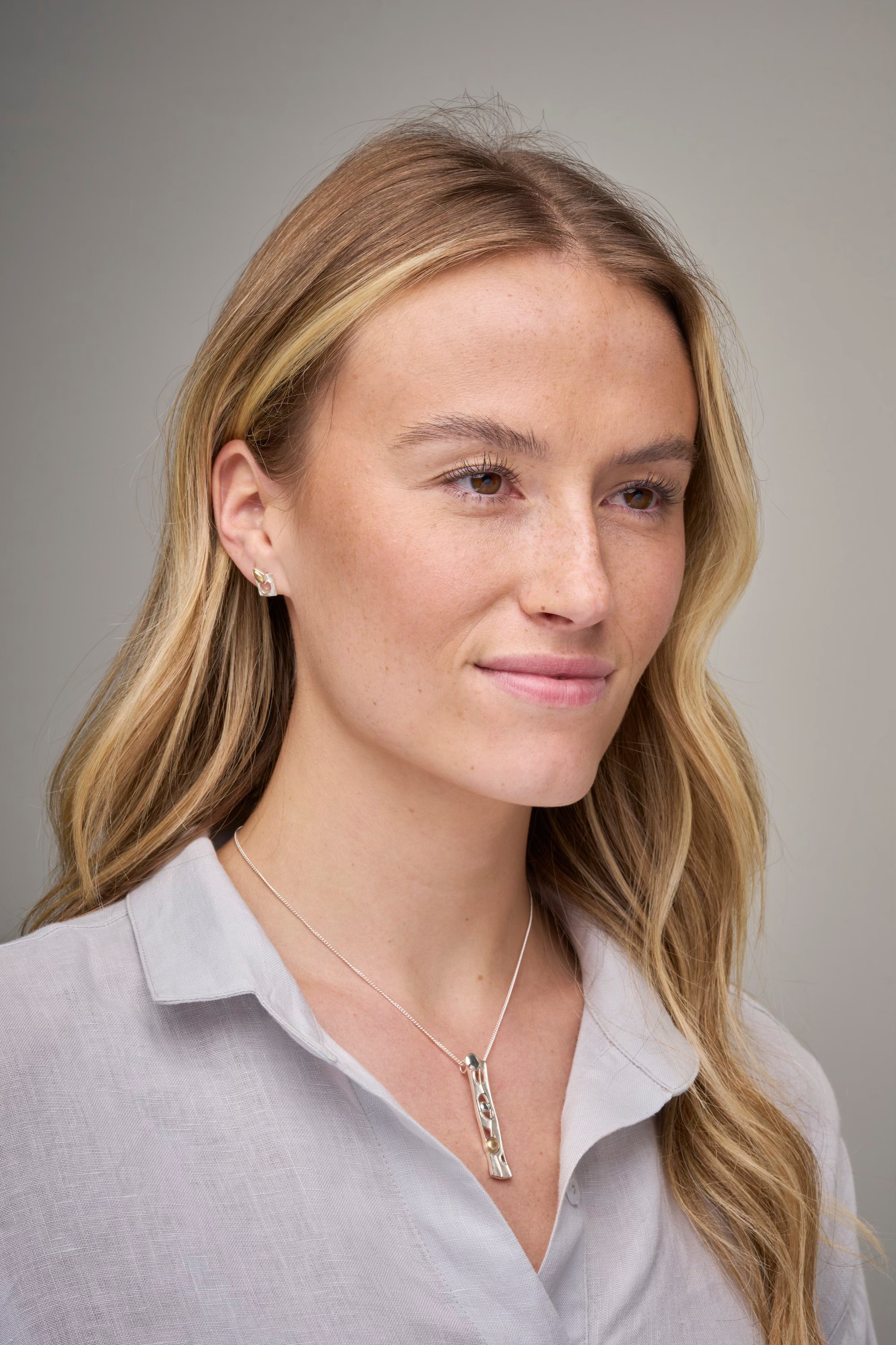 Woman in grey top with long necklace and studded earring