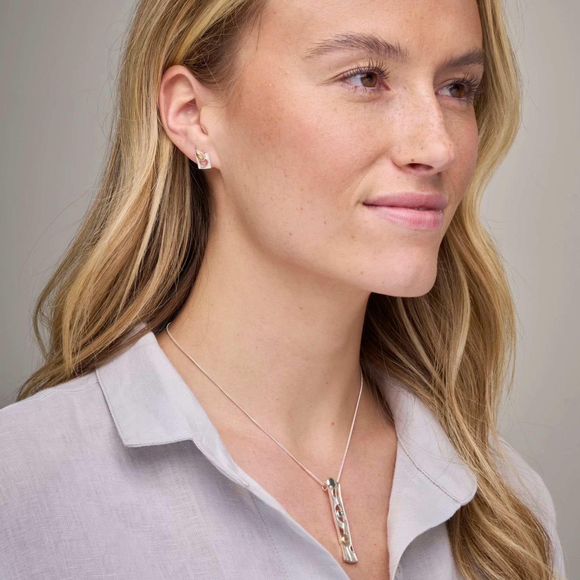 Woman in grey top with long necklace and studded earring