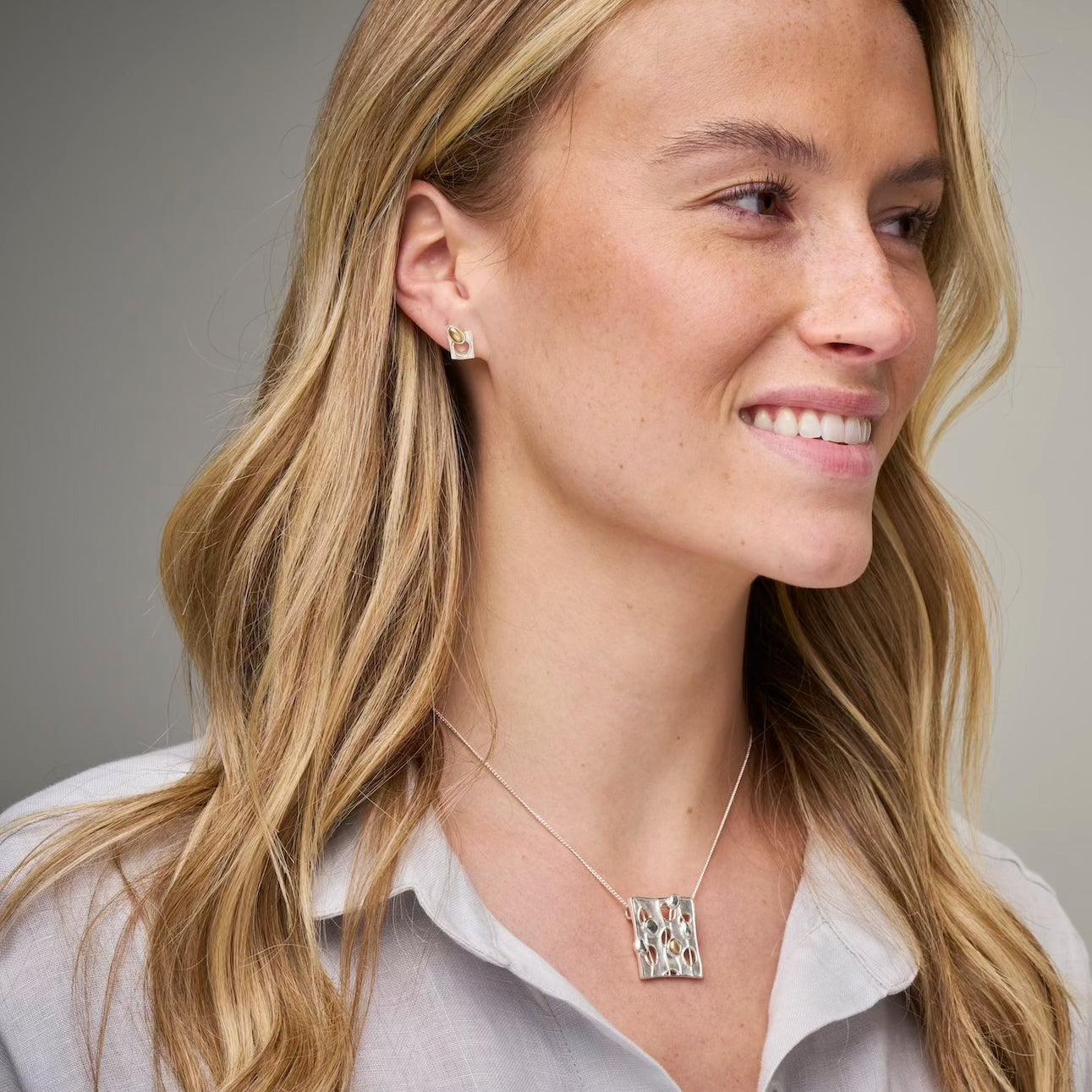 A woman wearing a white shirt and a necklace with a square mixed metal pendant.