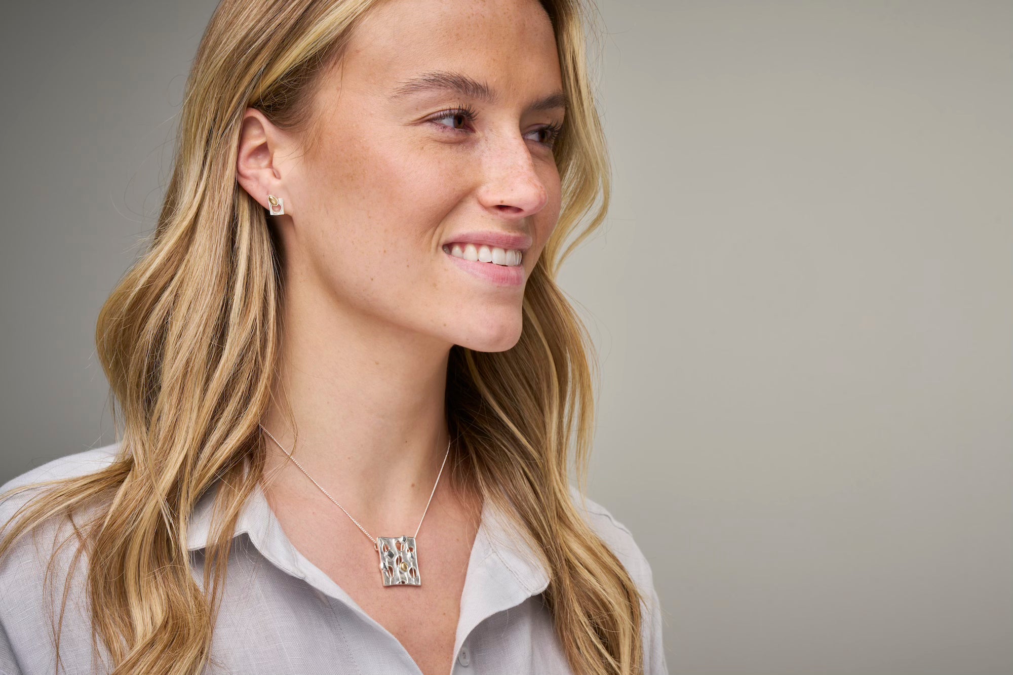 Woman in grey top with necklace and earrings