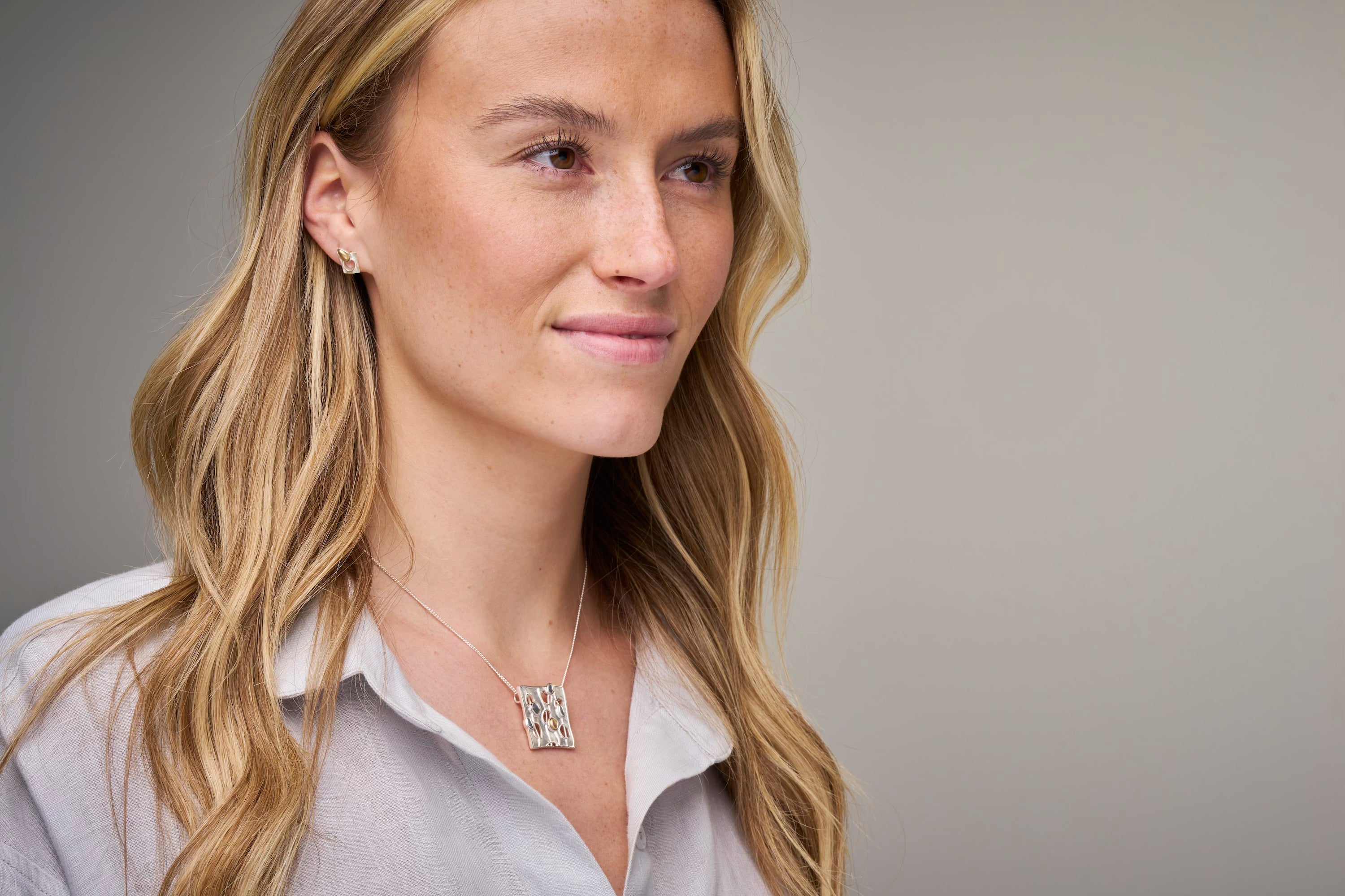 Woman in grey top with square necklace and studded earring