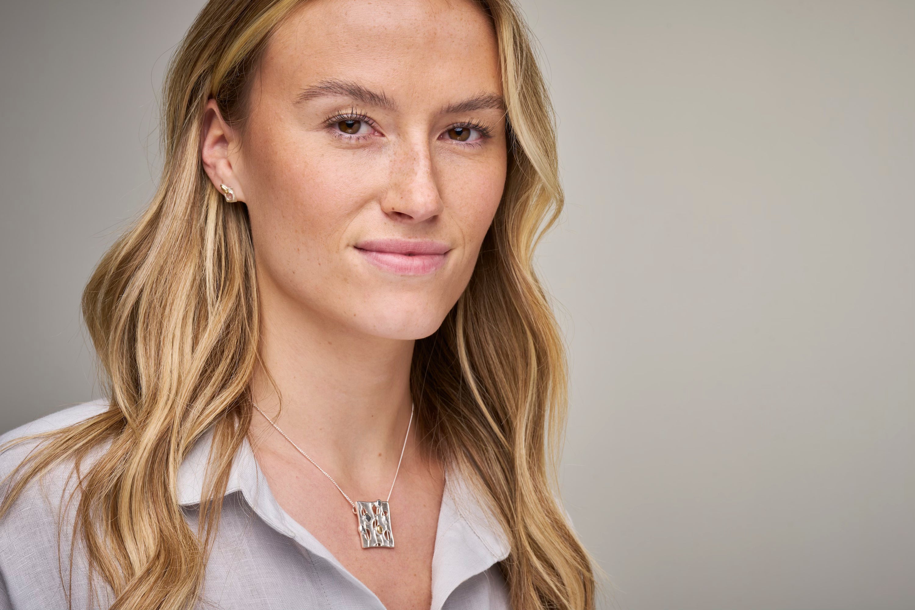 woman in grey top with necklace and earrings