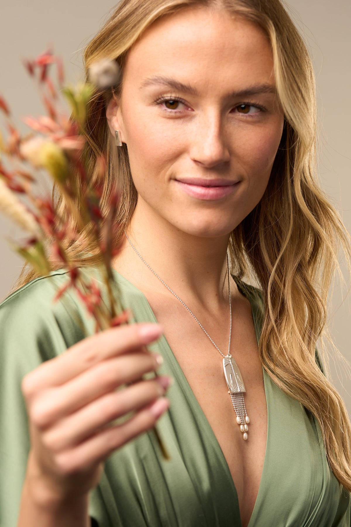 woman in green dress holding flower with necklace with bird design
