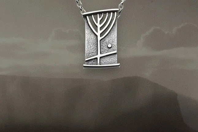 An image of a silver rectangular necklace with a rune design from the Ingibiorg Collection. Overlaid on a black and white image of the Hoy hills