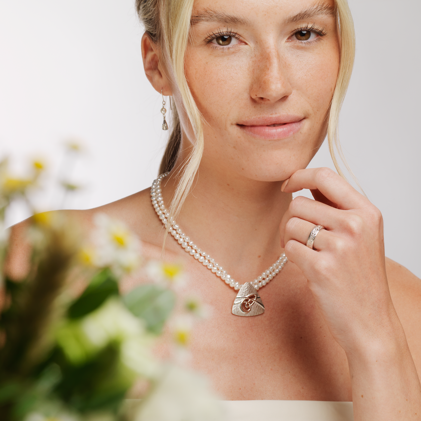 Woman in white top wearing a pearl and silver Aikerness necklace, matching earring and rysa ring