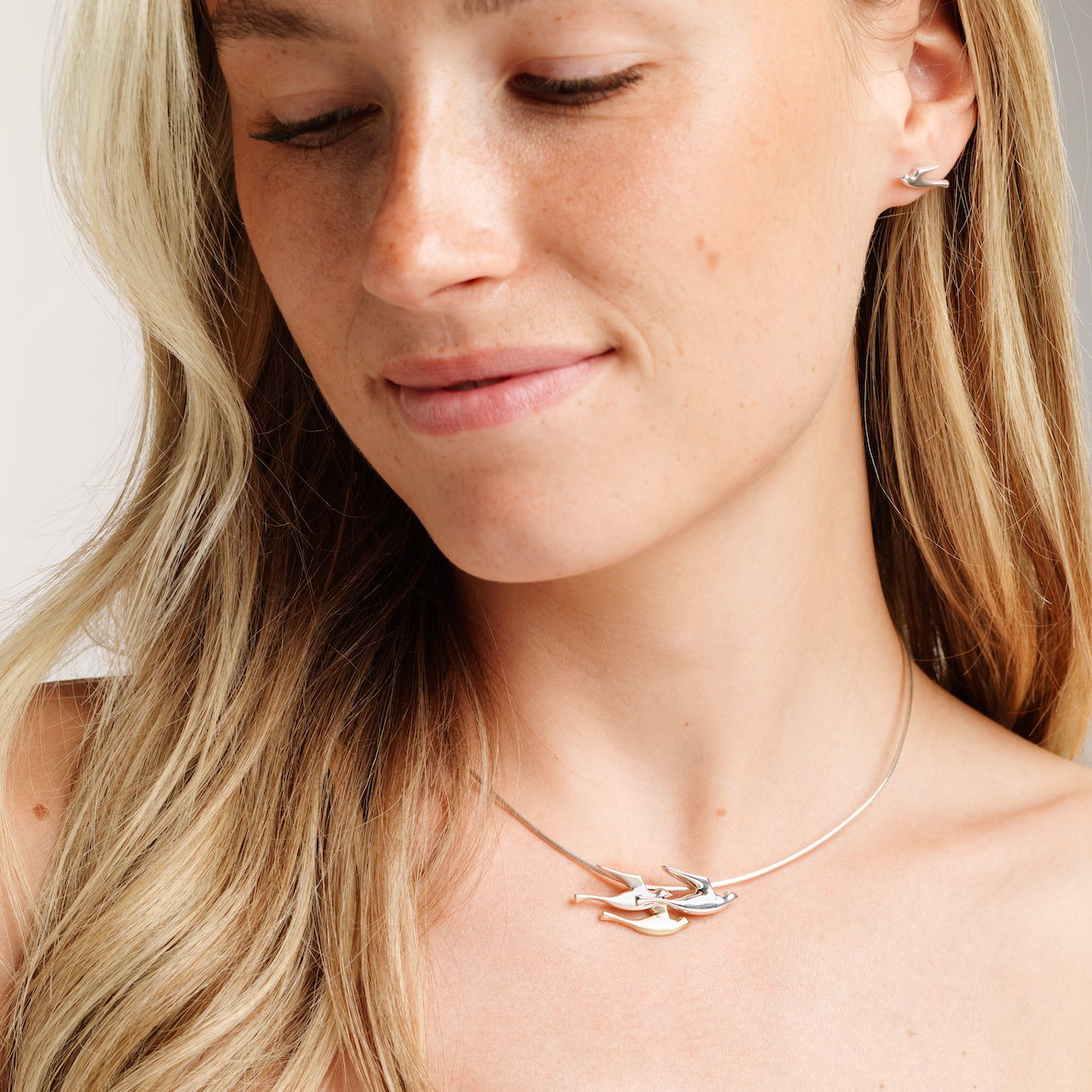 A woman wearing a silver birdland pendant necklace with matching stud earring
