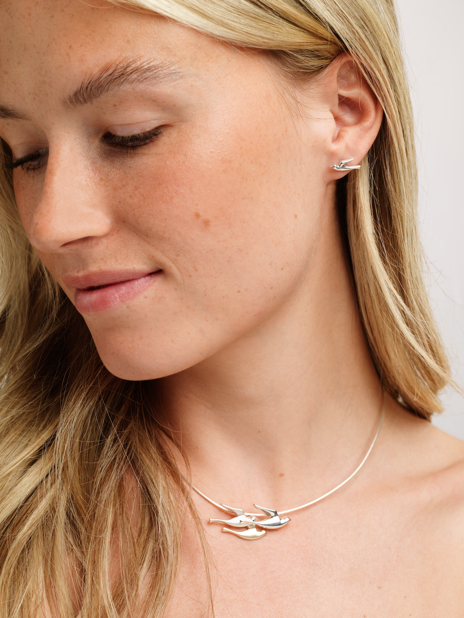 A woman wearing a silver birdland pendant necklace with matching stud earring