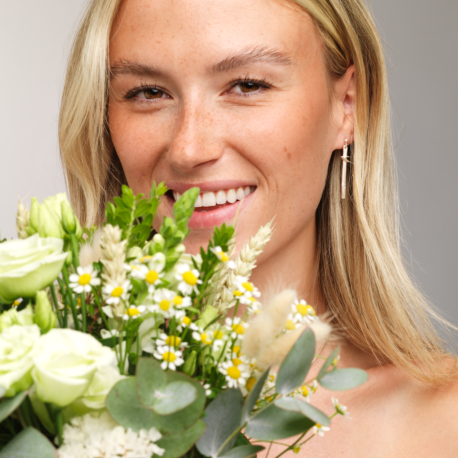 close up of woman with birdland drop earring and flowers in foreground