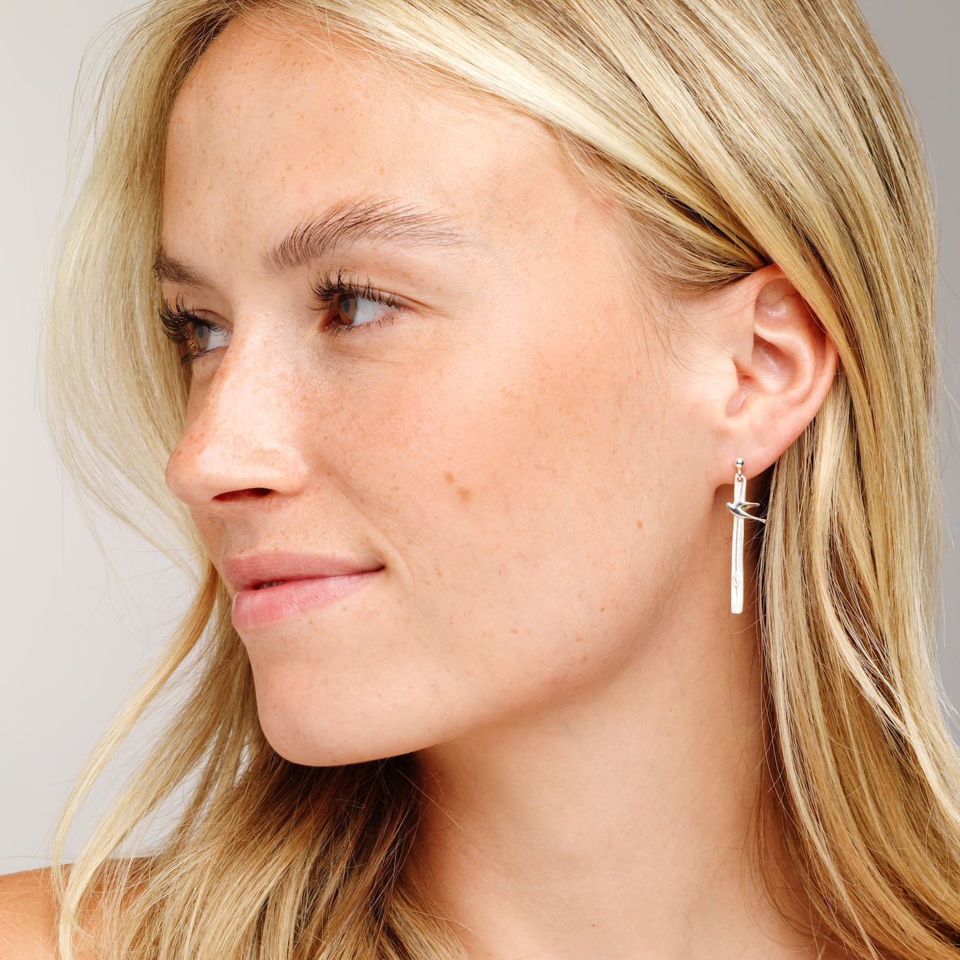 A close-up of a woman's ear wearing a silver birdland earring