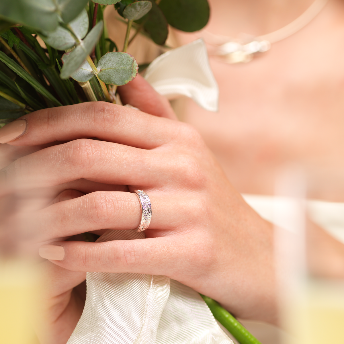 greenery has focus in foreground with ring in background woman is blurred wearing birdland necklace