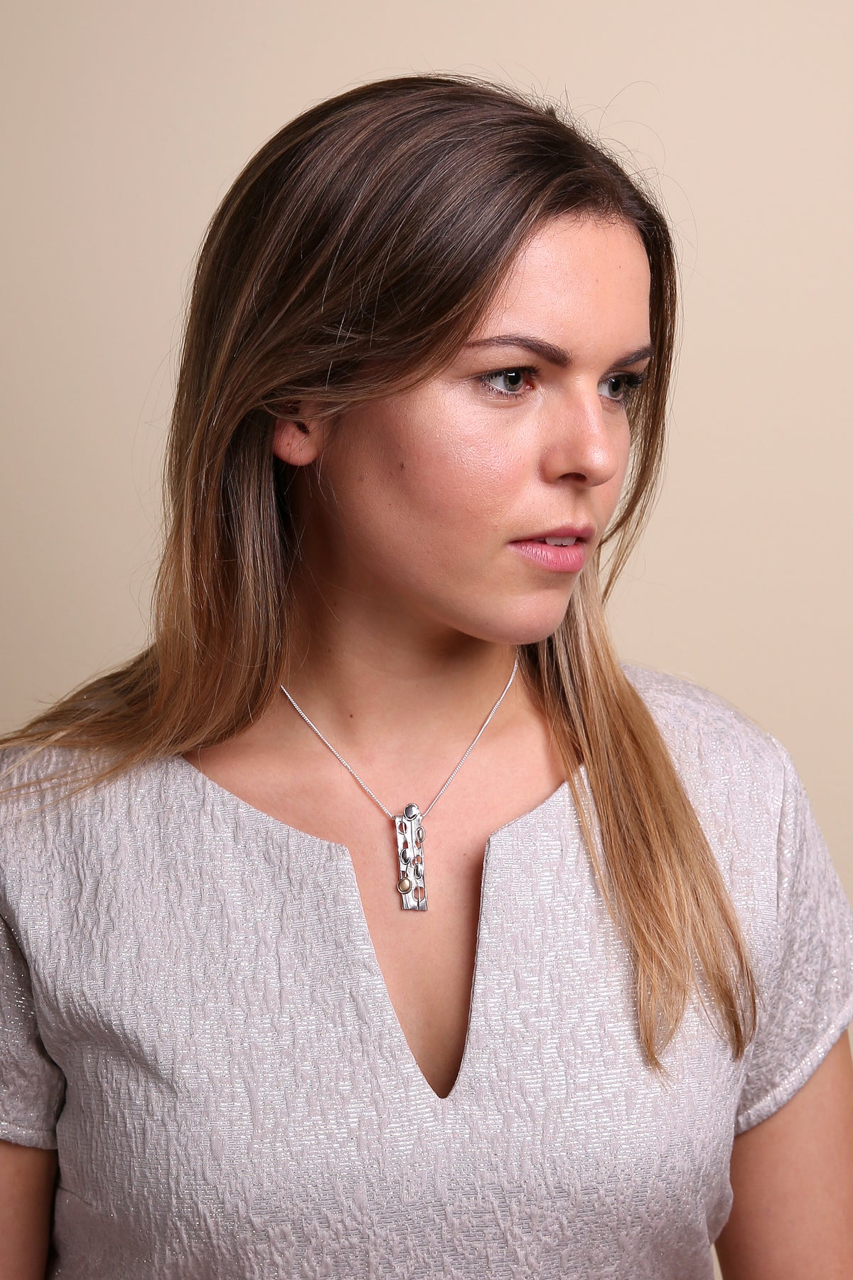 Woman in silvered coloured top is modelling a long silver pendant necklace from the Flow collection