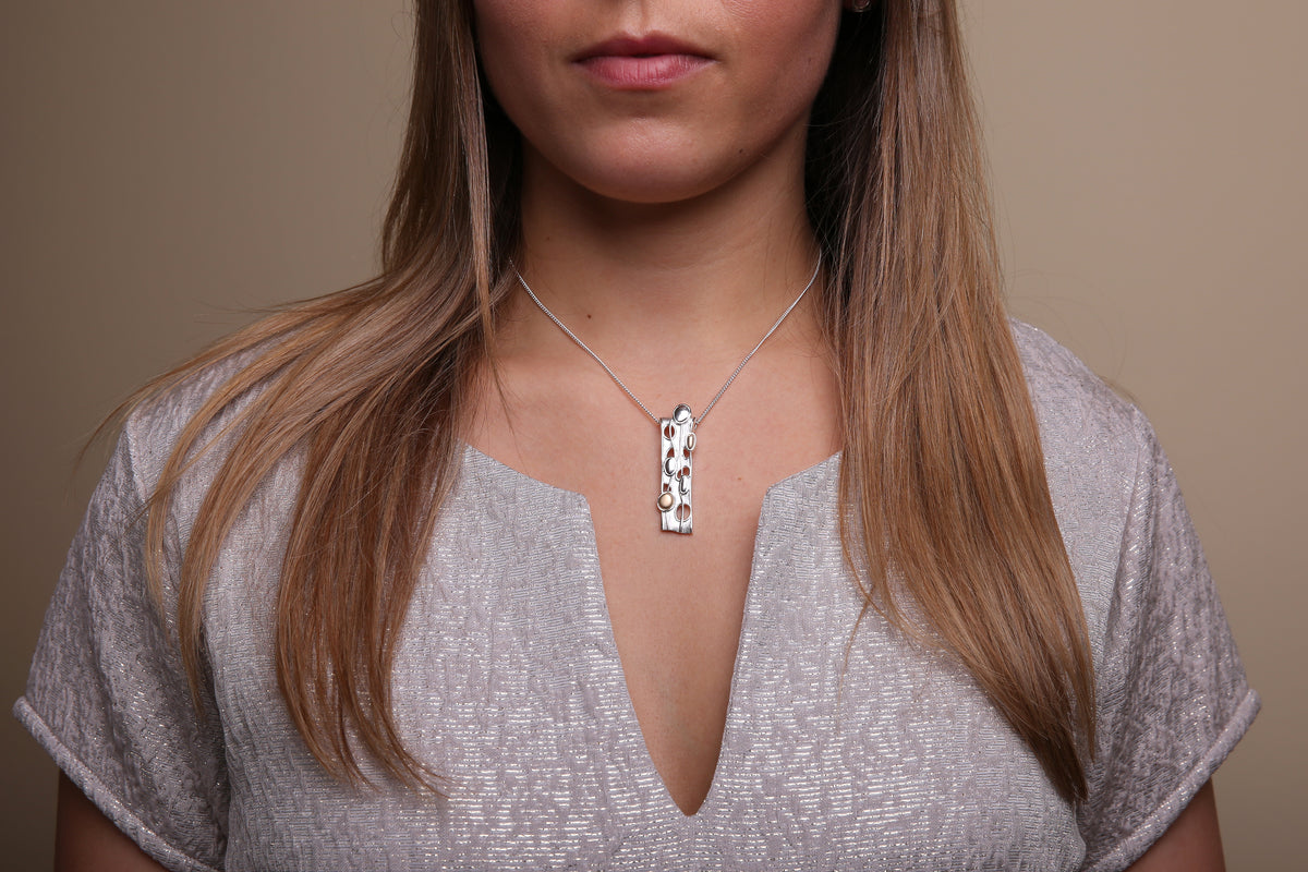 Woman in silvered coloured top is modelling a long silver pendant necklace from the Flow collection