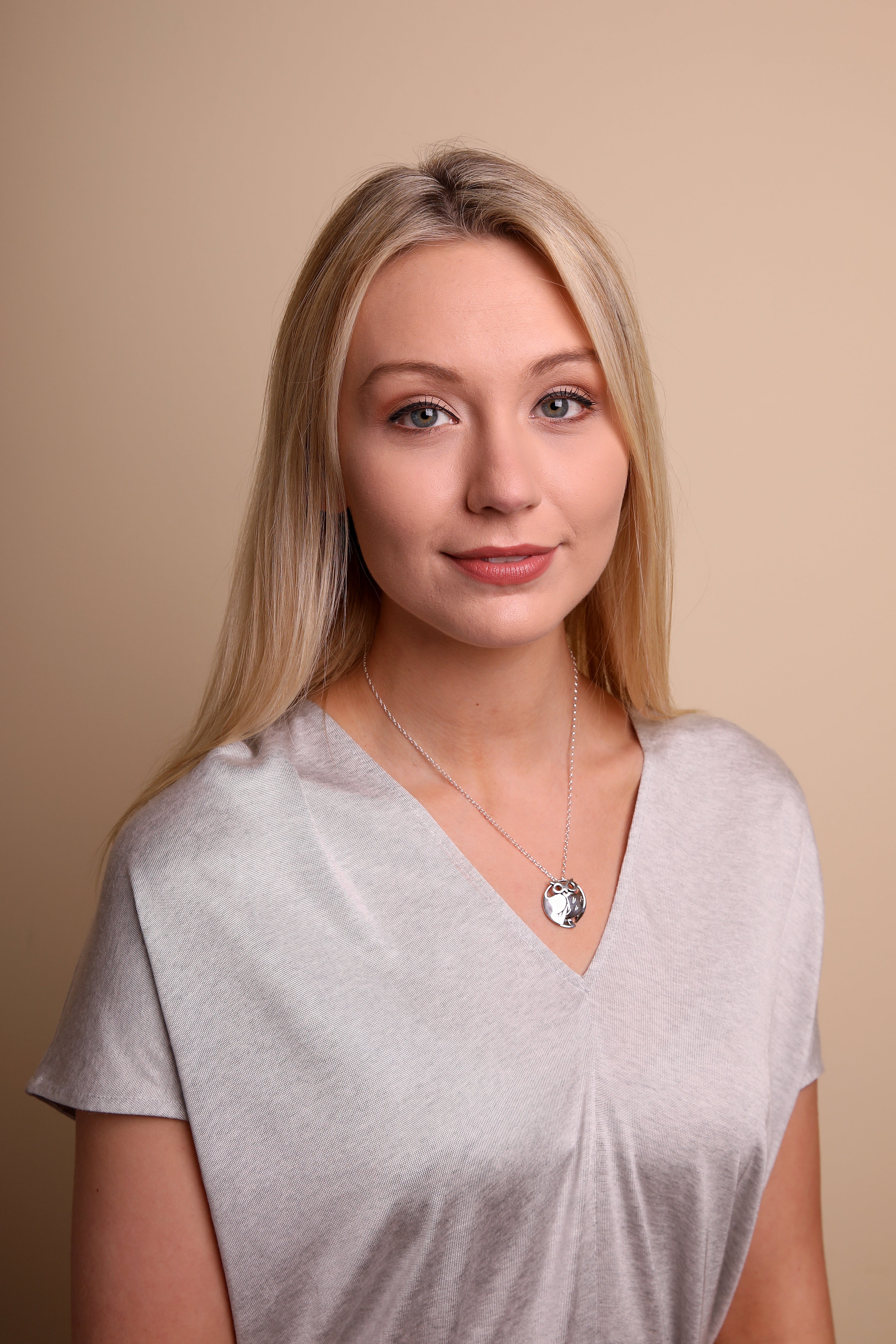 A woman wearing a grey top is modelling a silver necklace