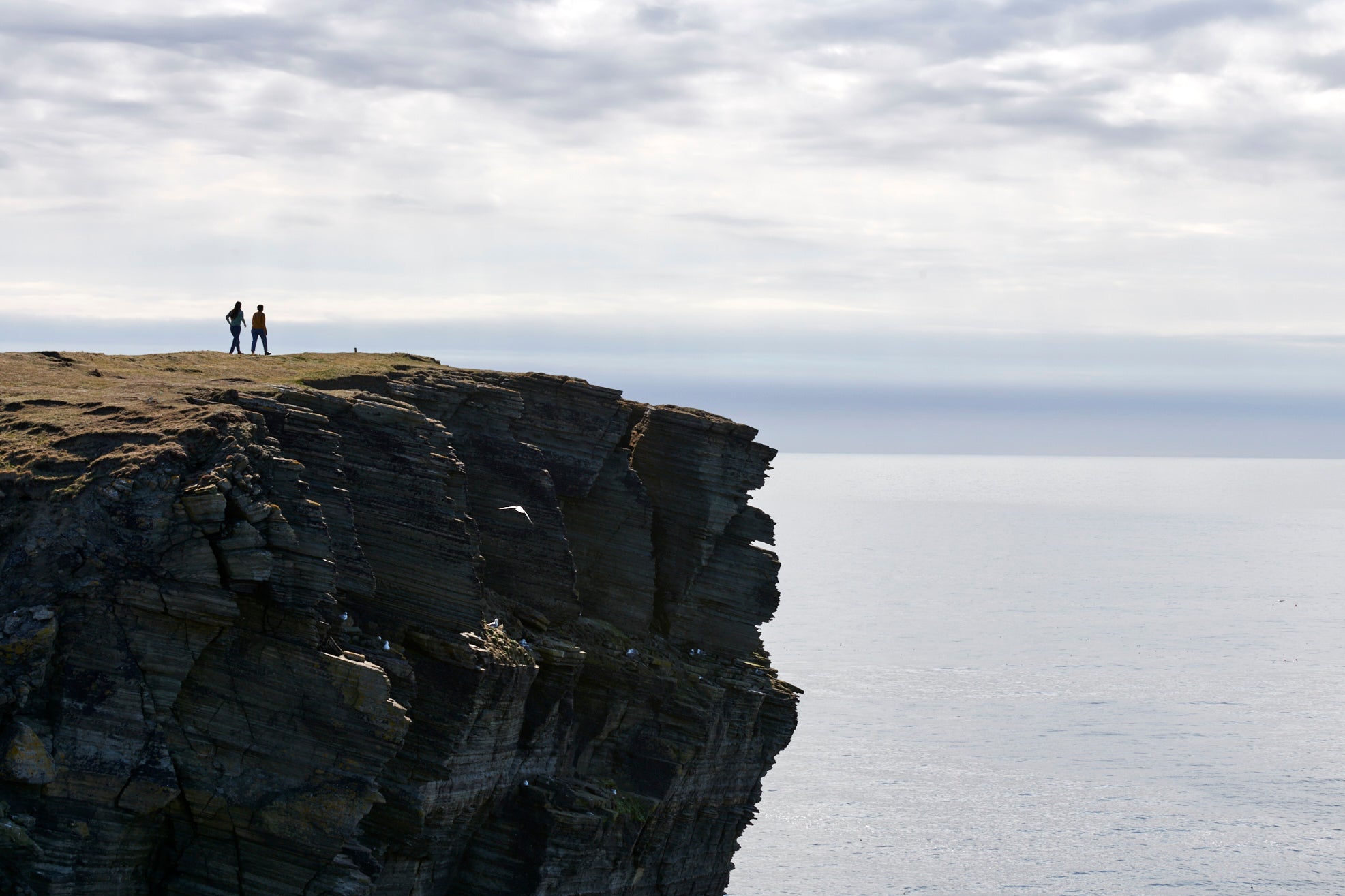 A scenic view of two people standing on a cliff overlooking the sea.
