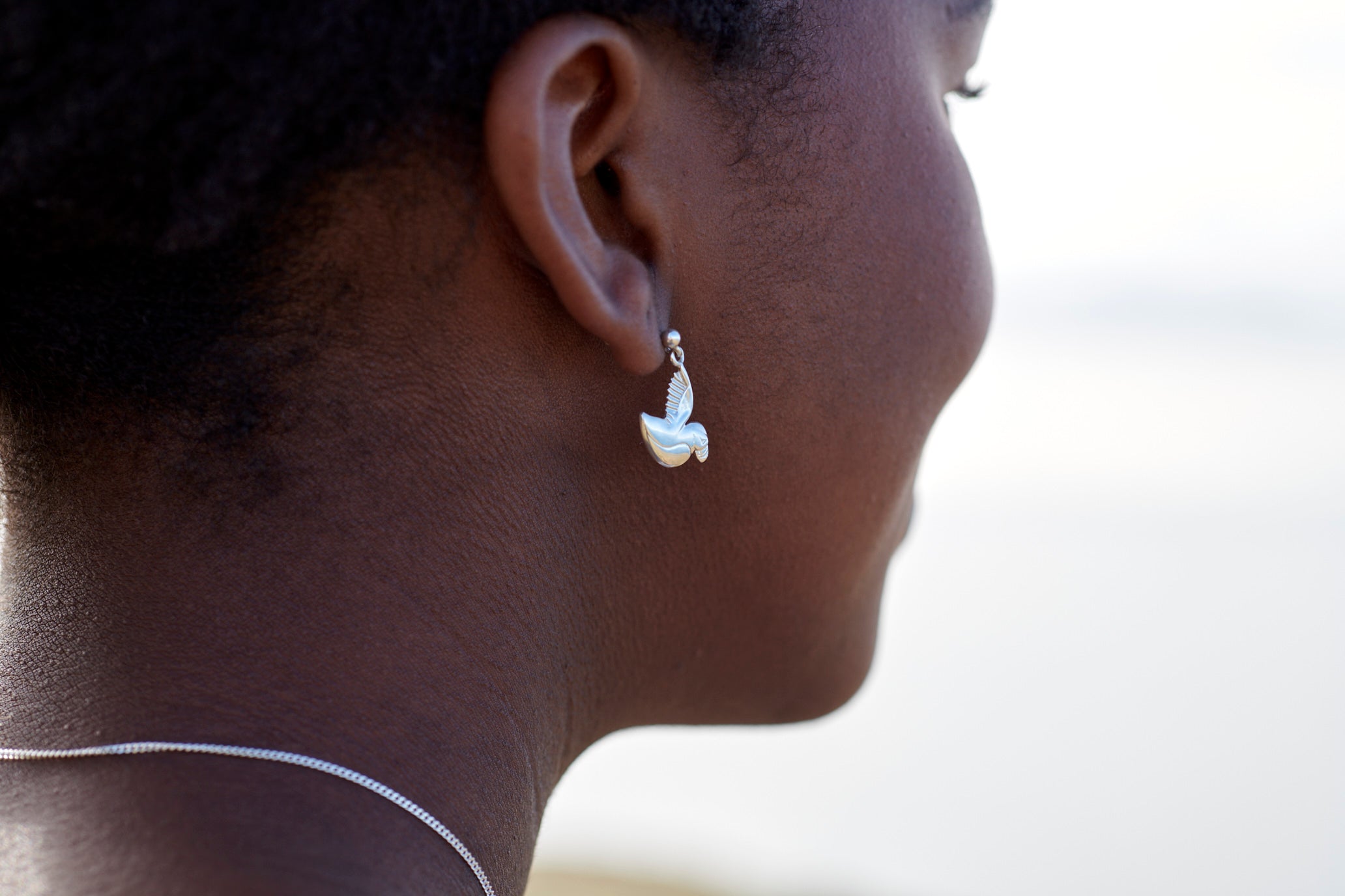 A close-up image of a person wearing a silver puffin drop earring.