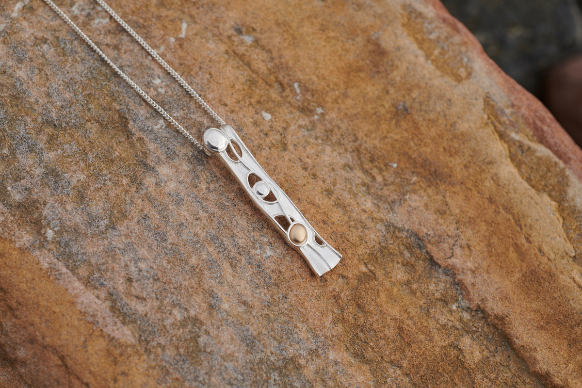 Close up of a silver Flow long pendant on a stone
