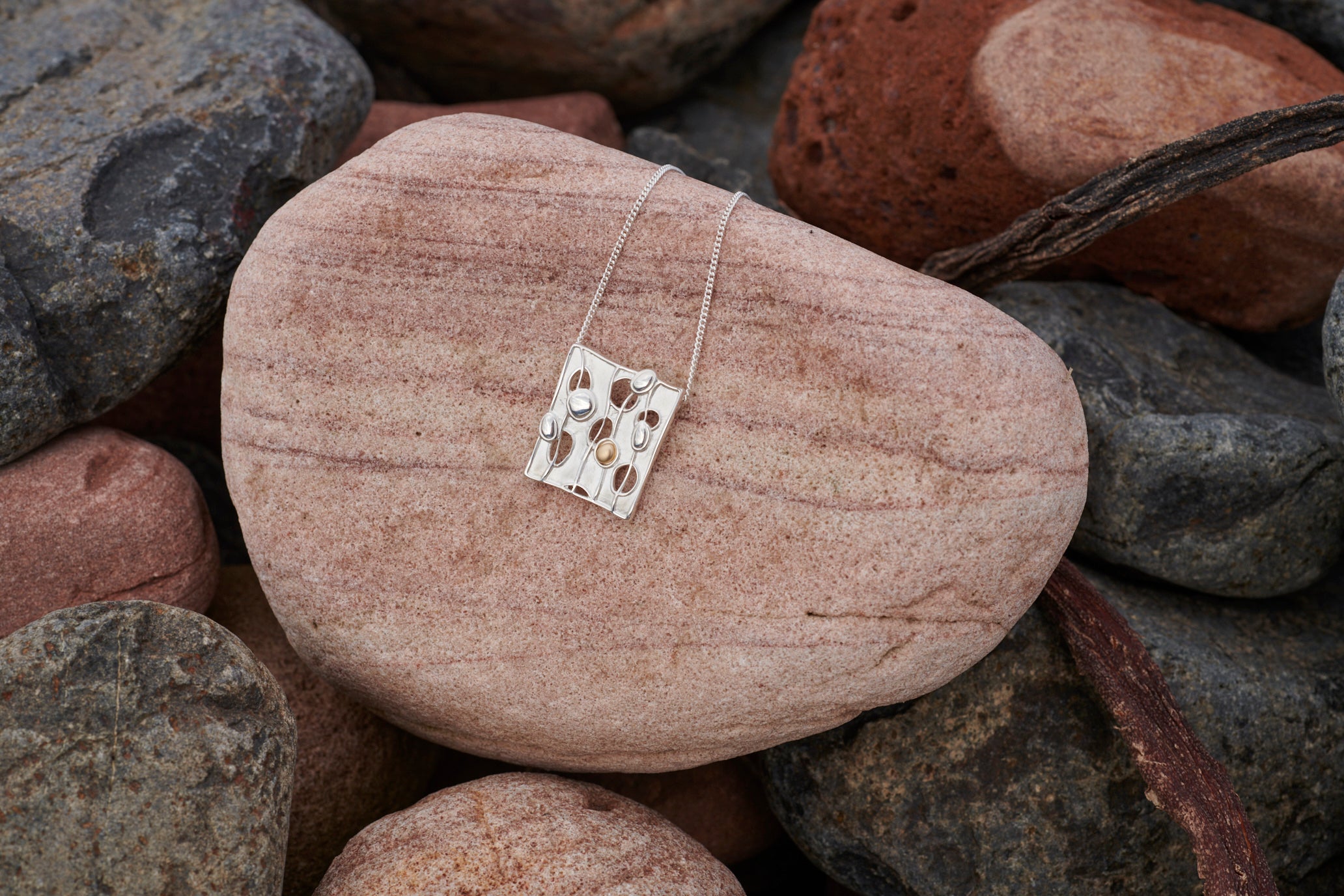 Close up of a silver Flow pendant on a stone