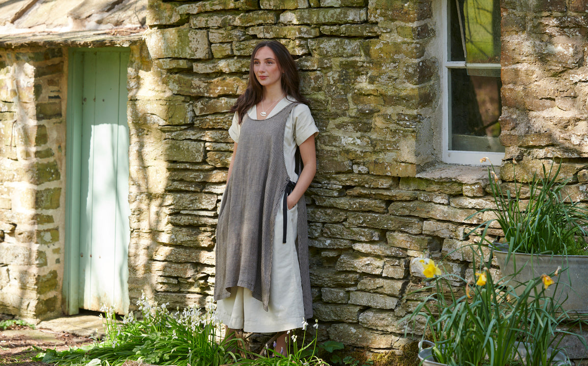 A woman is standing in front of a stone house modelling a necklace