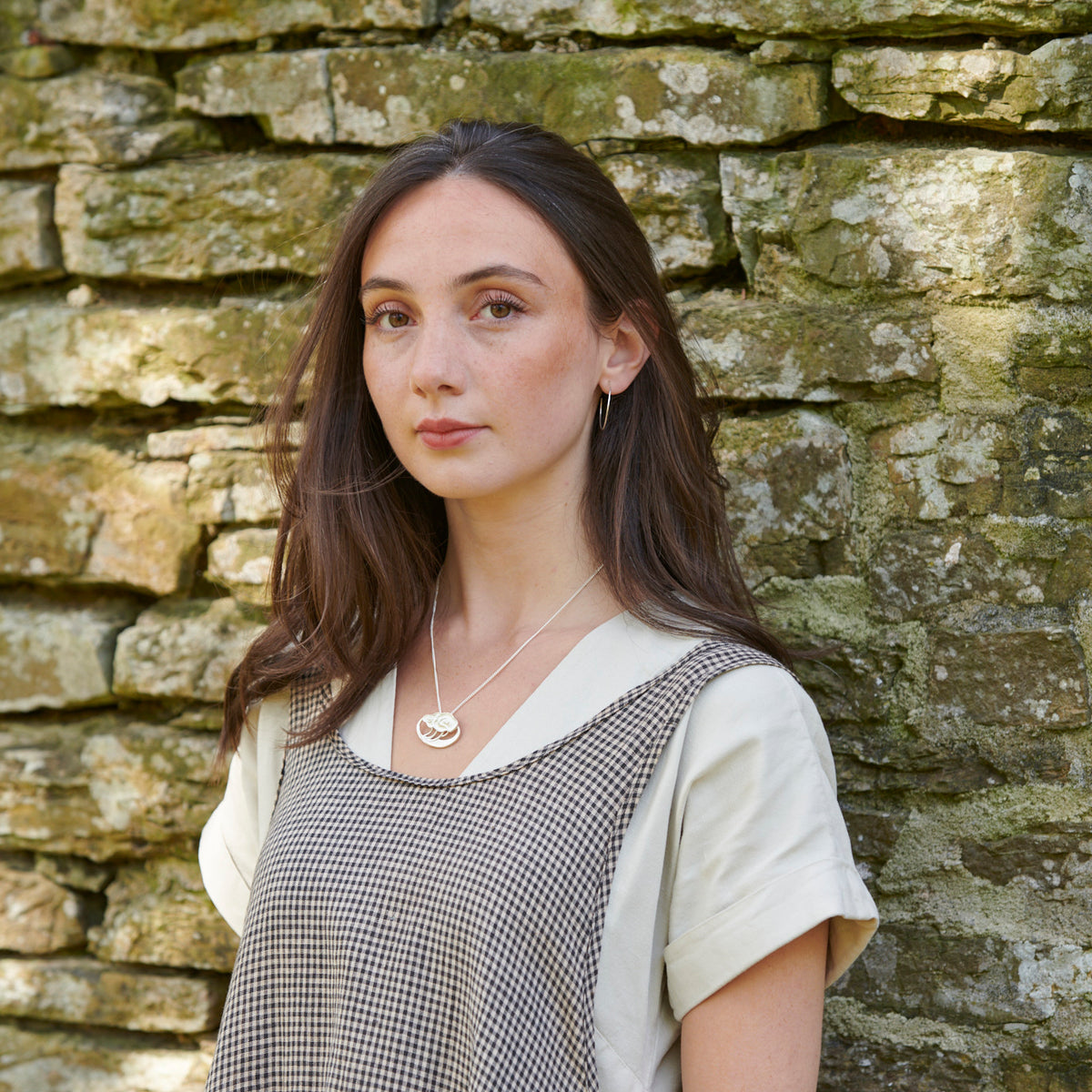 A woman is standing in front of a stone wall modelling a necklace