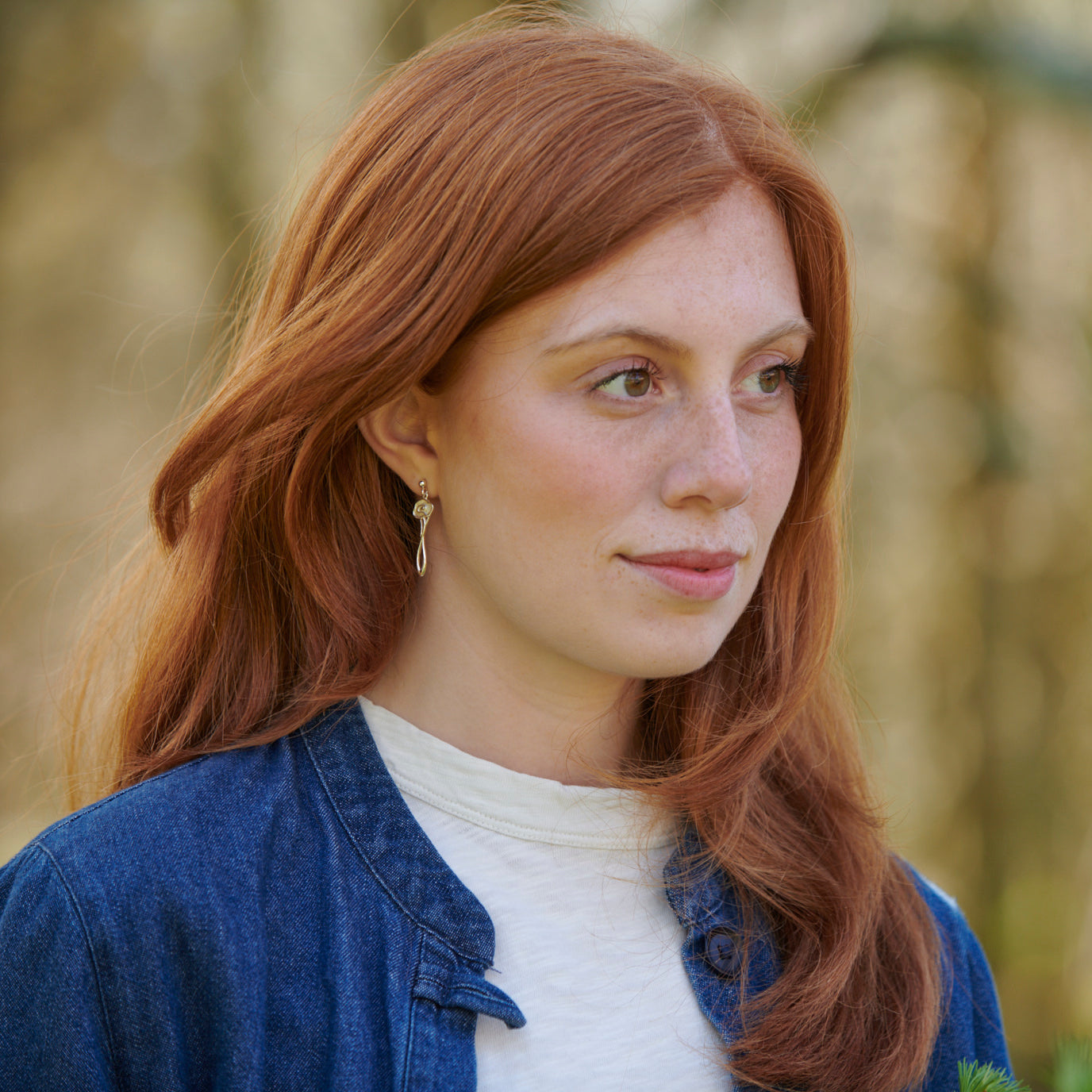 A woman in a wood modelling a brooch, background is blurred 