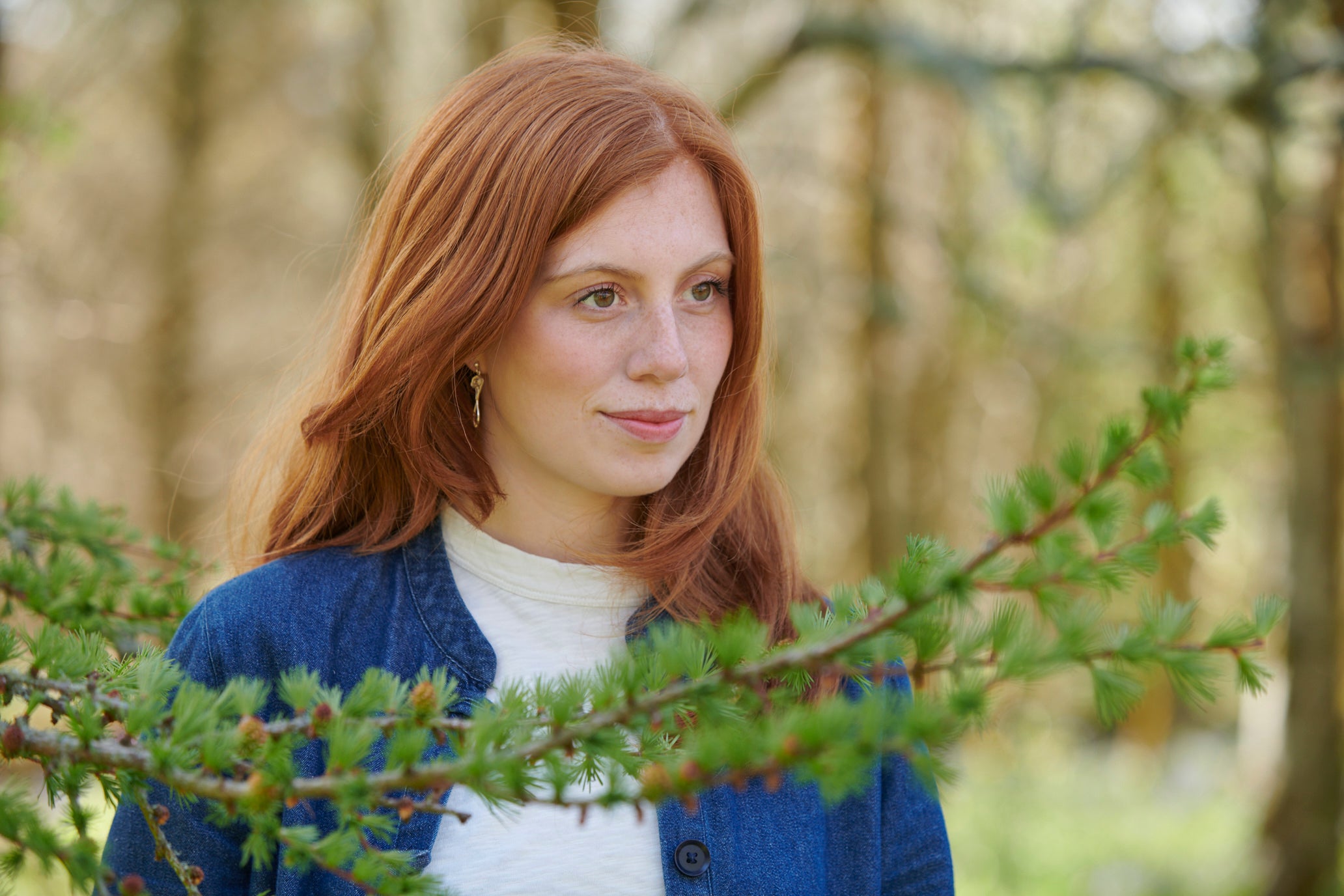 A woman is standing behind a branch modelling an earring