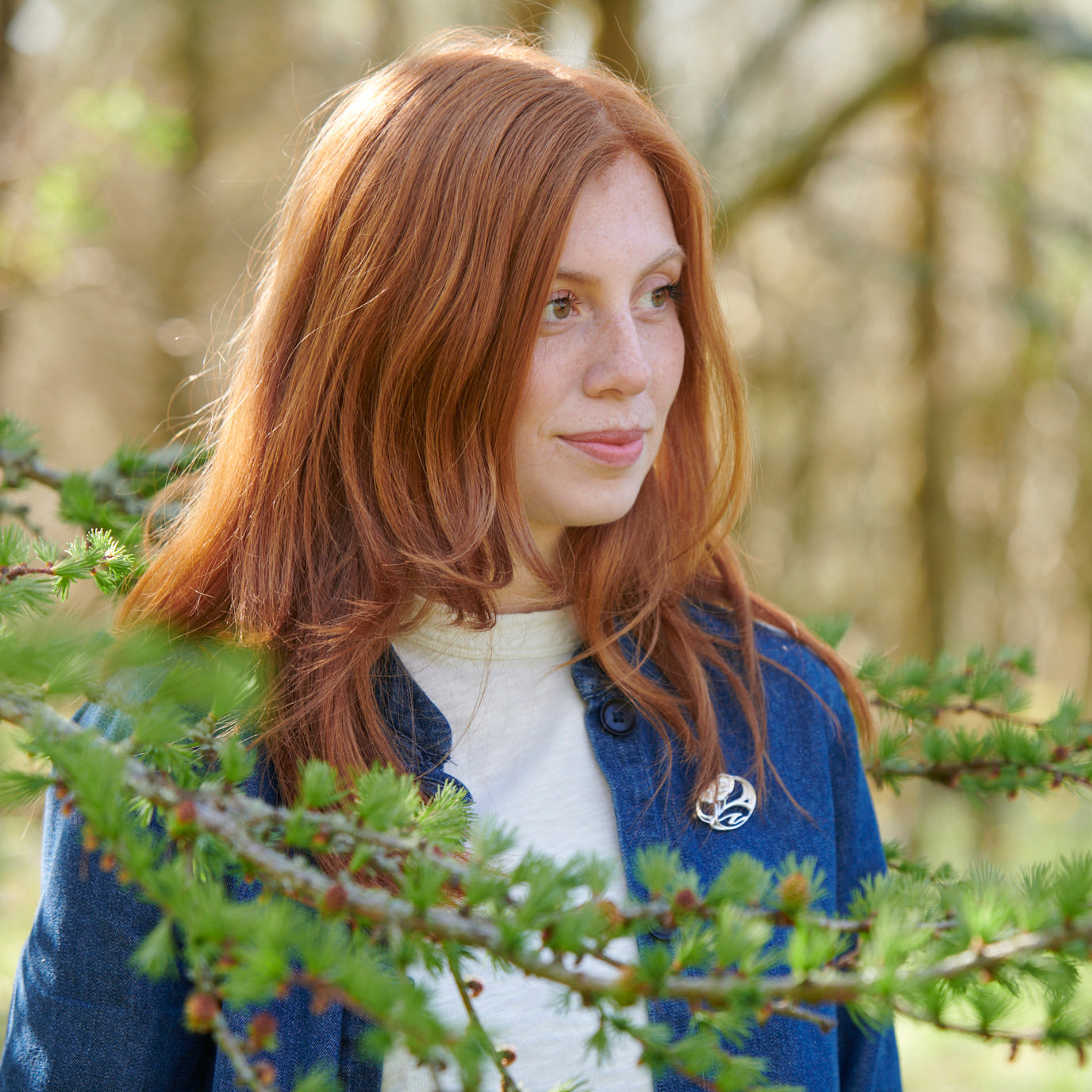 A woman is standing behind a branch modelling a brooch