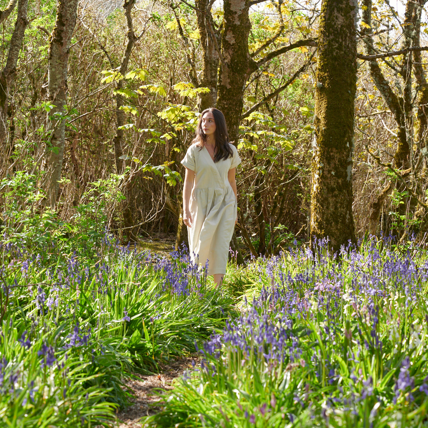 A woman in white dress is walking through a wood with bluebells