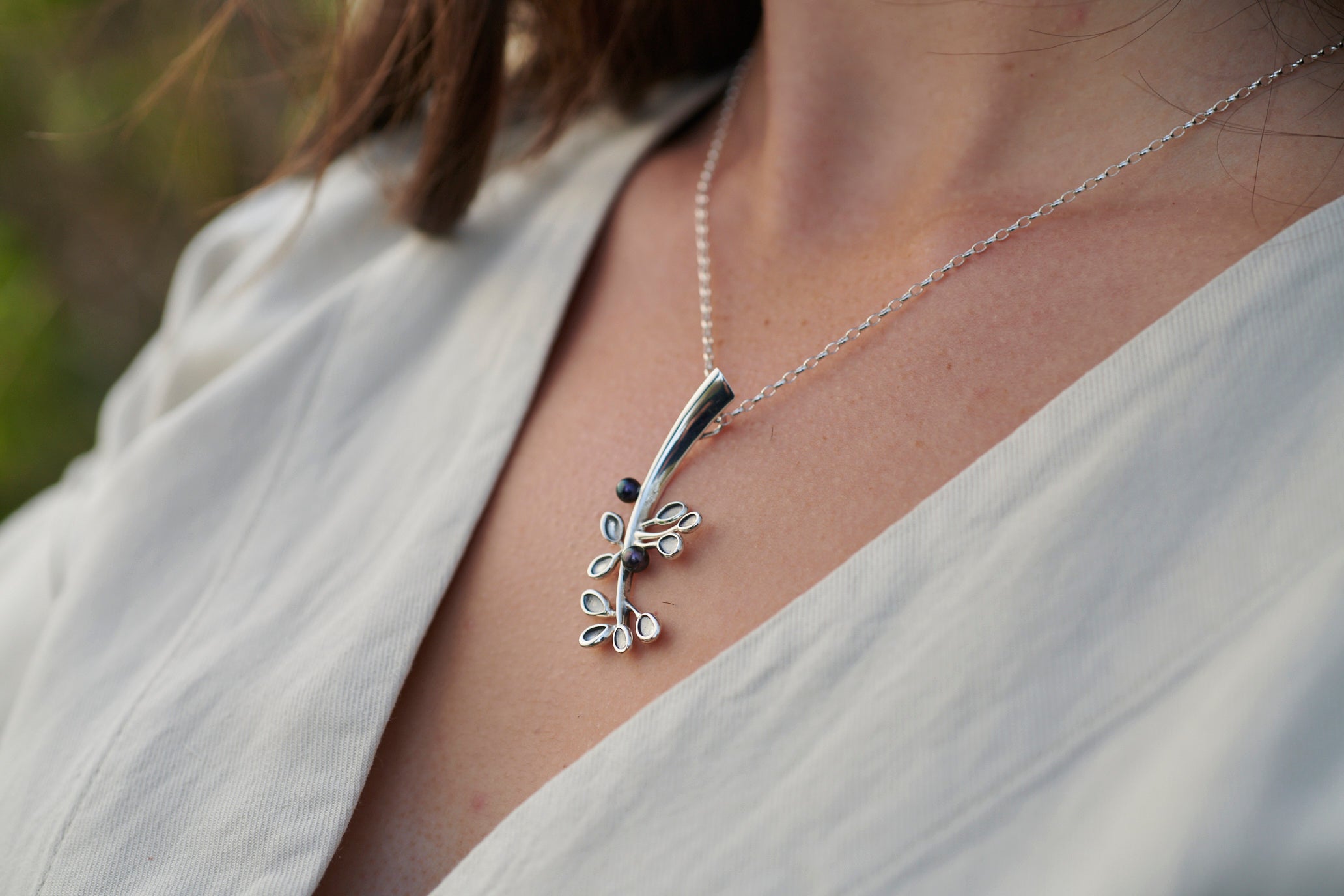A silver pendant featuring a stylized cloudberry on a necklace, worn by a person in a white shirt.