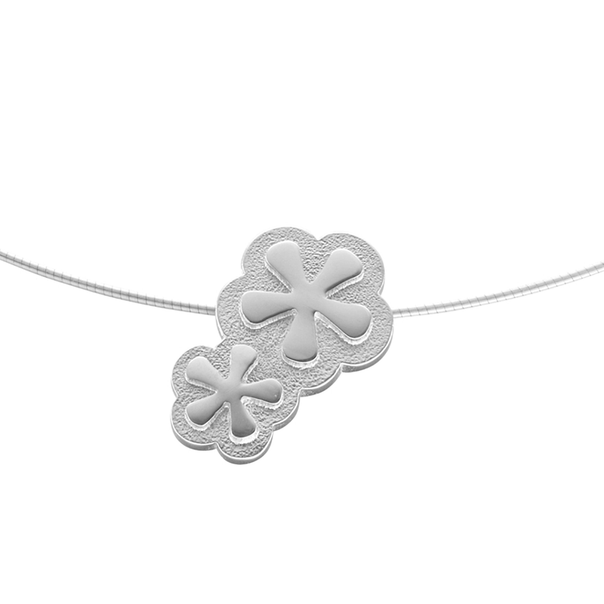 A silver necklace with a pendant that features two flowers linked to each other